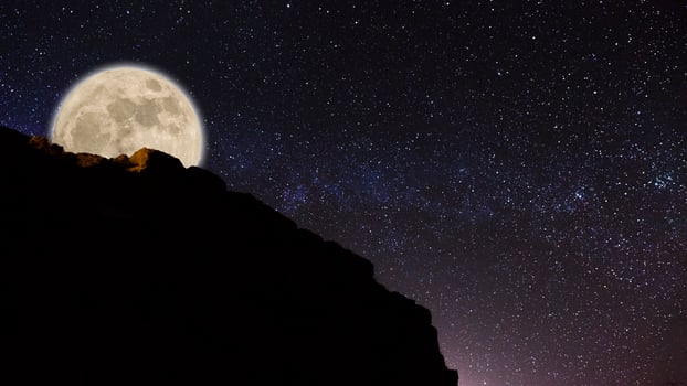 Low light and long exposure photography of the night sky with a mountain on the right. Grainy texture and soft-focus background. Night sky Milky way with full Moon and universe constellation in the ba photo
