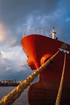 Low angle view of cargo ship docked at port against rain cloudy sky at sunset time in vertical frame photo