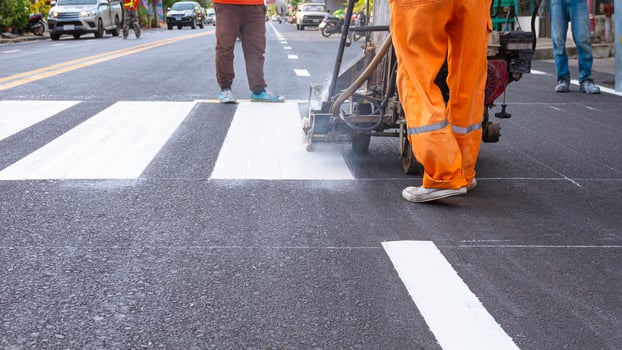 Low section of road workers group with thermoplastic spray marking machine are painting pedestrian crosswalk on asphalt road in the city photo