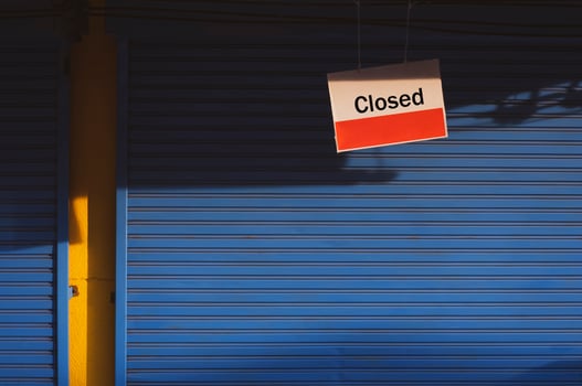 Hanging closed sign board in front of blue shutter door of grocery with sunlight and shadow on surface in vintage tone style photo