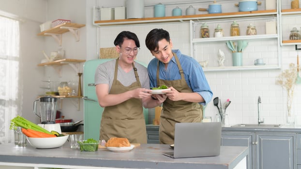 Young smiling gay couple cooking together in the kitchen at home, LGBTQ and diversity concept. photo