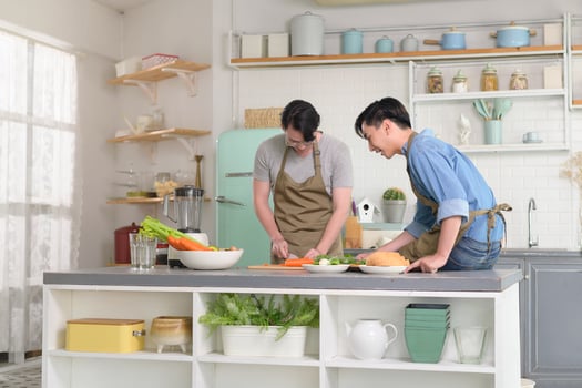 Young smiling gay couple cooking together in the kitchen at home, LGBTQ and diversity concept. photo