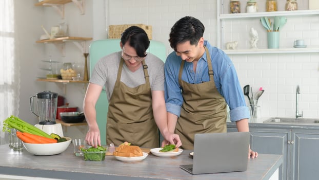 Young smiling gay couple cooking together in the kitchen at home, LGBTQ and diversity concept. photo