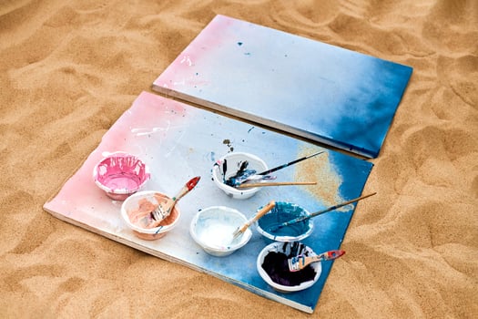 Two painted canvas with palettes of paints lying on sand, artist's palette at outdoor art festival photo
