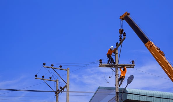 Two electricians with crane truck are installing electrical equipment on power pole against blue sky background photo