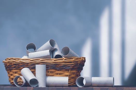 A lot of empty tissue roll cores in wicker basket on wooden table with blurred loft cement wall background, paper recycling and reuse concept photo
