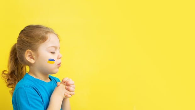 girl holding folded hands in prayer with yellow and blue colors of the Ukrainian flag on his cheek photo