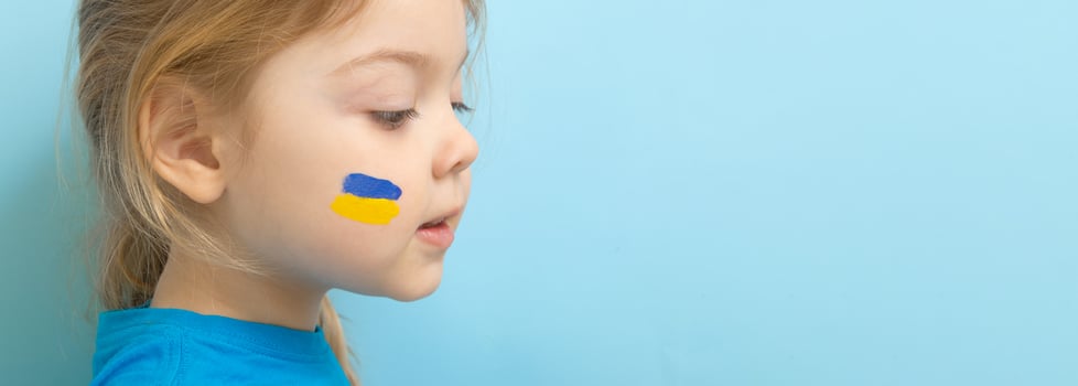 A girl with a painted Ukrainian flag of yellow and blue on her cheeks. Copy space on blue background photo