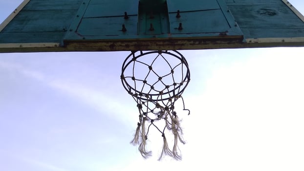 Bottom view of dim green old basketball hoop and broken net with a dark background of morning sky in the public sport field. photo