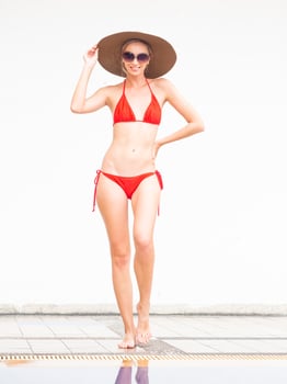 sexy girl happy girl in red bikini wear hat and sunglasses near swimming pool with white wall. photo