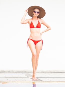 sexy girl happy girl in red bikini wear hat and sunglasses near swimming pool with white wall. photo