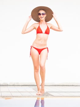 sexy girl happy girl in red bikini wear hat and sunglasses near swimming pool with white wall. photo