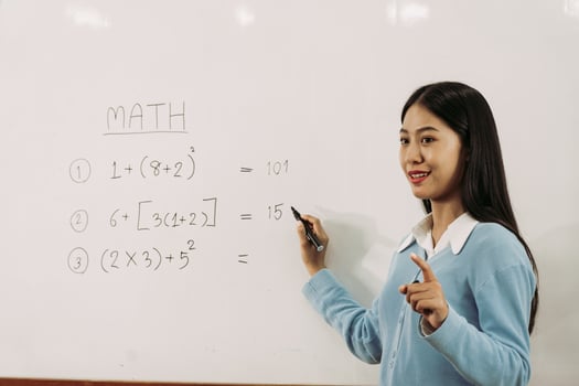 Asian female teacher is teaching students at the classroom while pointing at numbers on the white board. photo