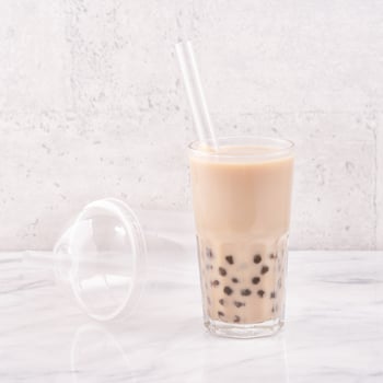Tapioca pearl ball bubble milk tea, popular Taiwan drink, in drinking glass with straw on marble white table and wooden tray, close up, copy space. photo
