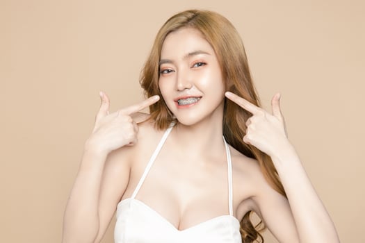 Cute young Asian woman wearing braces is feeling happy with clean fresh skin isolated over cream background. Plastic surgery Face care, Facial treatment, Cosmetology, beauty and spa, Women portrait. photo