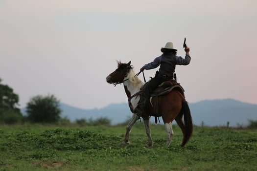 Cowboy riding horse with hand holding gun against sunset background. photo