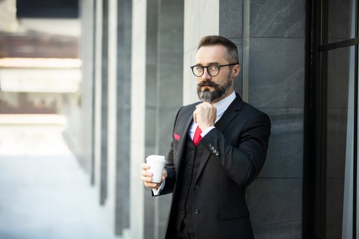 Hipster businessman in suit standing with coffee cup near office outdoor photo