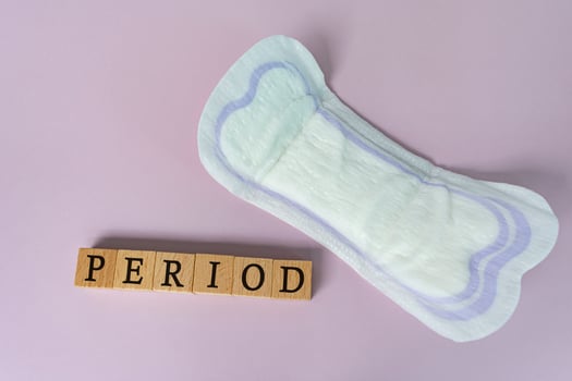 Period text on wooden block. Sanitary pads on purple background. Top view. photo