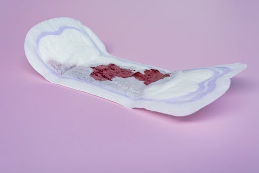 Menstrual blood on a sanitary pad on pink background. Flat lay photo