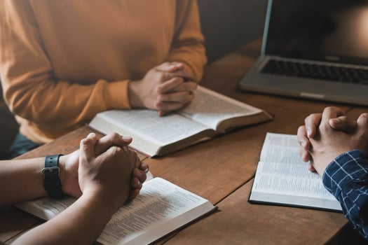 A group of Christians sit together and pray around a wooden table with blurred open Bible pages in their homeroom. Prayer for brothers, faith, hope, love, prayer meeting photo