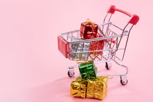 Annual sale, Christmas shopping season concept - mini red shop cart trolley full of gift box isolated on pale pink background, copy space, close up photo