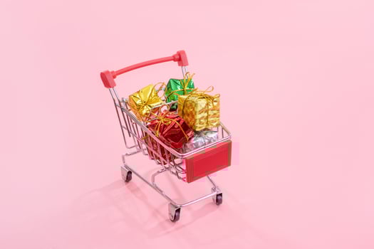 Annual sale, Christmas shopping season concept - mini red shop cart trolley full of gift box isolated on pale pink background, copy space, close up photo
