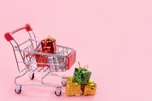 Annual sale, Christmas shopping season concept - mini red shop cart trolley full of gift box isolated on pale pink background, copy space, close up photo