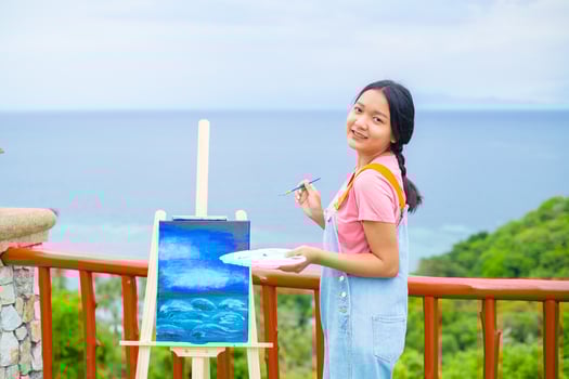 Young girl using brush drawing picture on canvas paper, at beautiful landscape view at koh tao Thailand. photo