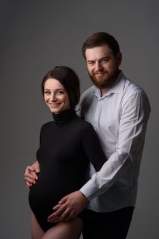 A pregnant woman and her husband are hugging on a gray background. Couple expecting a baby. photo