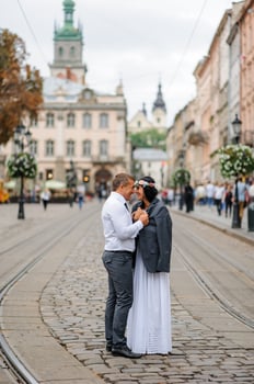 Wedding photo session on the background of the old building. The groom watches his bride posing. Rustic or boho wedding photography.