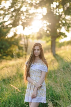 Portrait of a young beautiful girl in a sundress. Summer photo session in the park at sunset. A girl sits under a tree in the shade.