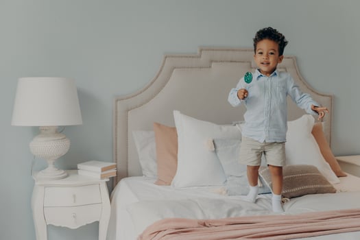 Carefree cute afro american child boy with lollipop jumping ob bed at home photo