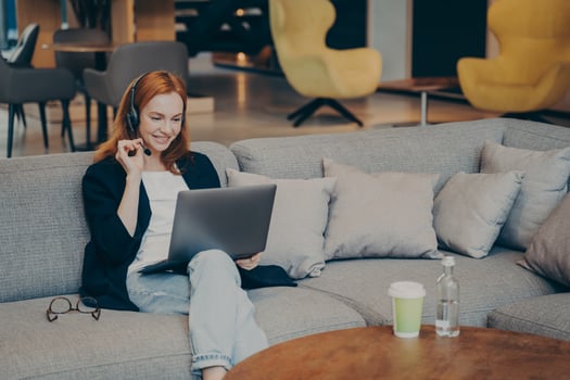 Positive female student doing part-time job works remotely using laptop and wireless headset photo