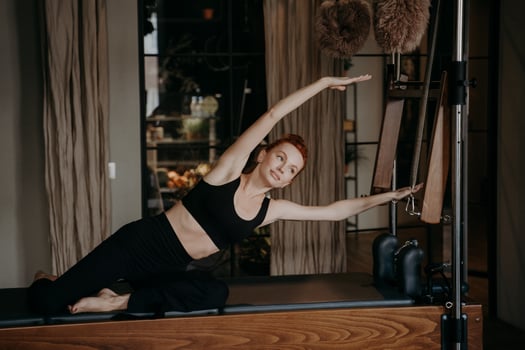 Young female pilates instructor exercising and stretching on cadillac reformer photo