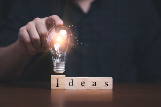 Hand touching to glowing lightbulb on ideas wording which print screen on wooden cube block for creative thinking idea and problem solving concept photo