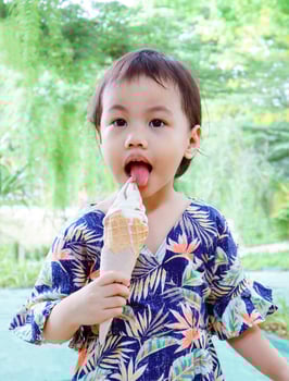 3 years old cute baby Asian girl sticking out her tongue and licking ice cream outdoor. photo