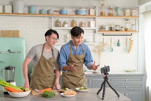 Young two close friend bloggers preparing food in the kitchen while live streaming via smartphone. photo