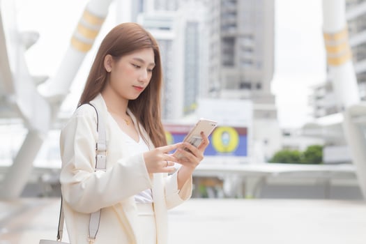 Beautiful young Asian business woman is going to the office or workplace which  holds smartphone in her hands in big city with business buildings with the city as a background. photo