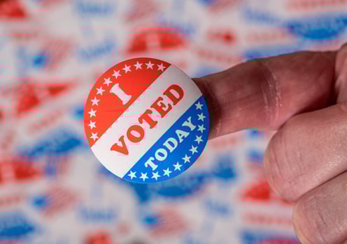 Finger with I Voted Today sticker in front of background created from many election voting badges photo