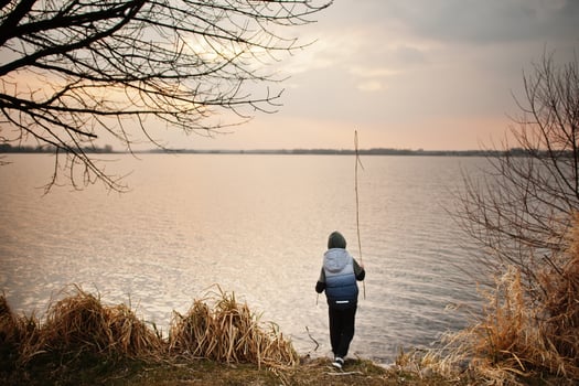 Boy in hoodie by the lake with a reed in his hands. photo
