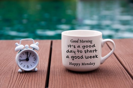 White alarm clock on wooden floor with morning quote text on coffee cup - It's a good day to start a good week. With blurred swimming pool background. photo