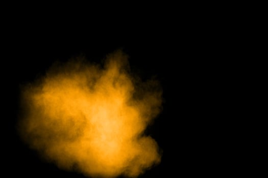 Abstract explosion of orange dust on black background. Freeze motion of orange powder splashing. photo