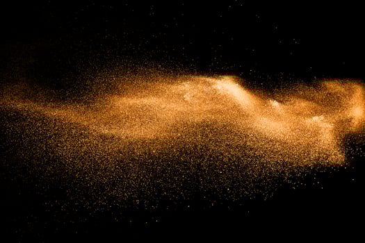 orange dust particles explosion on black background. Color powder dust splash. photo