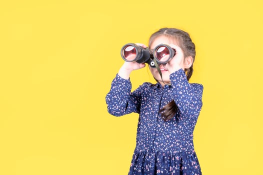 A cute girl raises a binoculars to look at the outside world through the lens photo