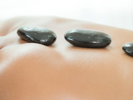 An expert masseuse at a spa salon puts hot stone on the back of an Asian woman to relieve tension from work photo
