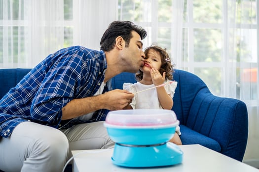 Caucasian family young father kissing his little daughter at mouth after eat cotton candy together on sofa at new house photo