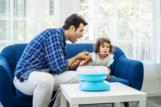 Hand father rolling cotton candy in candy floss machine and eat cotton candy together with daughter on sofa at new house photo