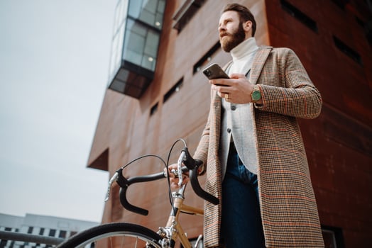 Young man with bicycle holding a smartphone front of building. Creative businessman in a modern business area. photo