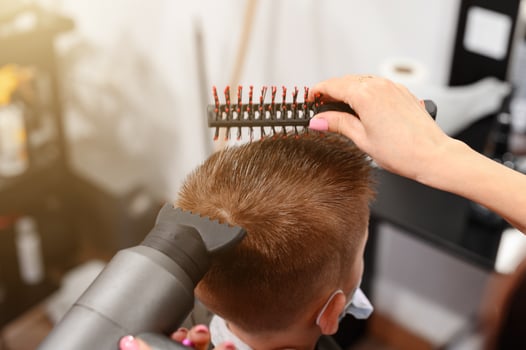 The hairdresser dries and styles the hair with the help of a hair dryer and a comb for a schoolboy boy, visiting the hairdresser during a coronavirus pandemic. photo
