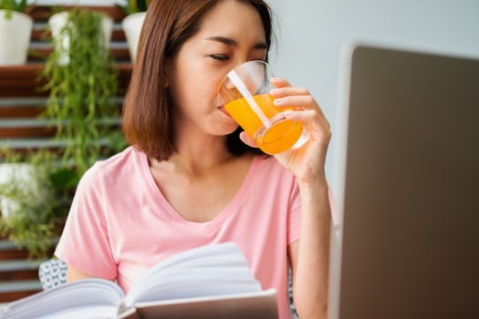 Mid-age Asian woman reading a book and hold orange juice glass in the home. Concept of  Health care And eating for healthy photo
